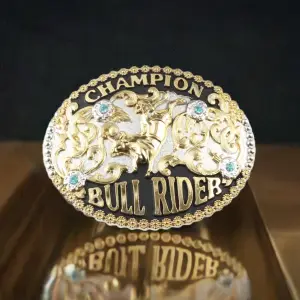 Golden oval Champion Bull Rider Belt Buckle with a gold bull and rider in the centre and text CHAMPION BULL RIDER and three blue stones to set it off.