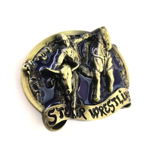 Steer Wrestling Belt Buckle. 3D Oval belt buckle with deep blue enamel surrounding a cowboy hanging from his running horse to catch and wrestle a running steer. The buckle has a ribbon across the bottom with the words STEER WRESTLING scribed in black enamel.