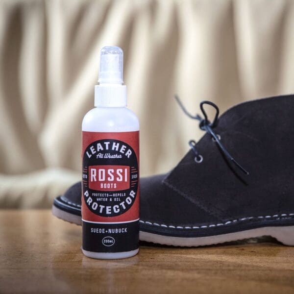 Rossi Boots Suede/Nubuck Protector Spray Display photo with sample brushed suede shoe on cream background, positioned on polished timber surface.